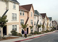 Exterior streetscape of the three-story gabled buildings at Hayes Valley, with cream, pink and grey stucco exteriors facing the sidewalks and front planting beds.